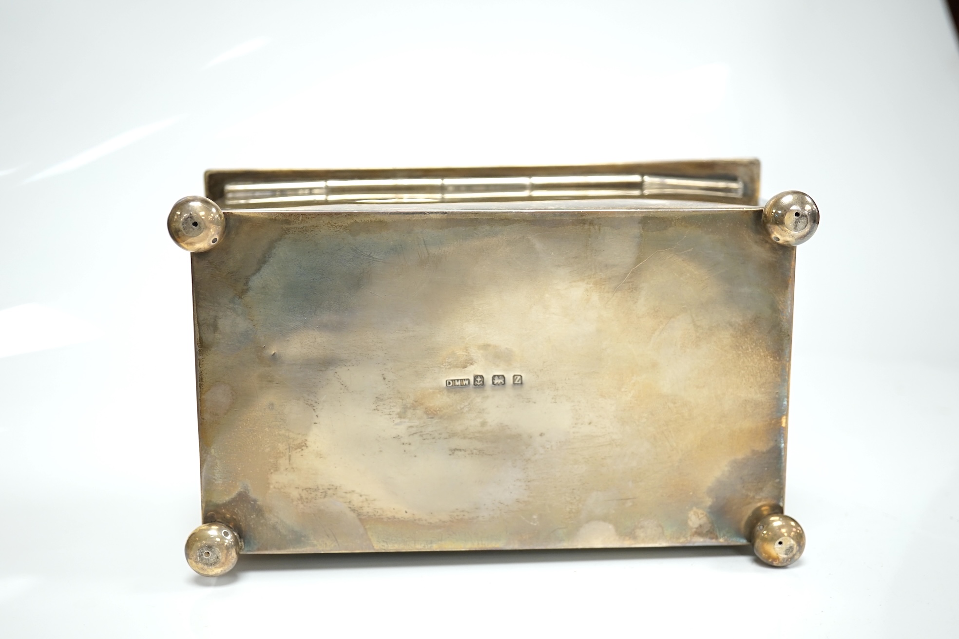 A George V Arts & Crafts silver mounted rectangular cigarette box, by Dryad Metal Works, Birmingham, 1924, on ball feet, the cover initialled ES, 15.2cm. Condition - fair